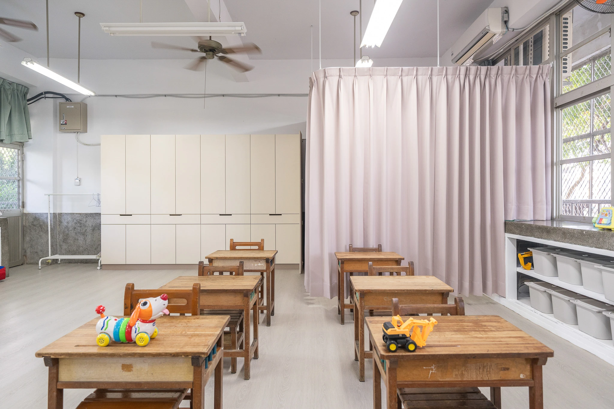 Wooden classroom desks beside a soft pink curtain