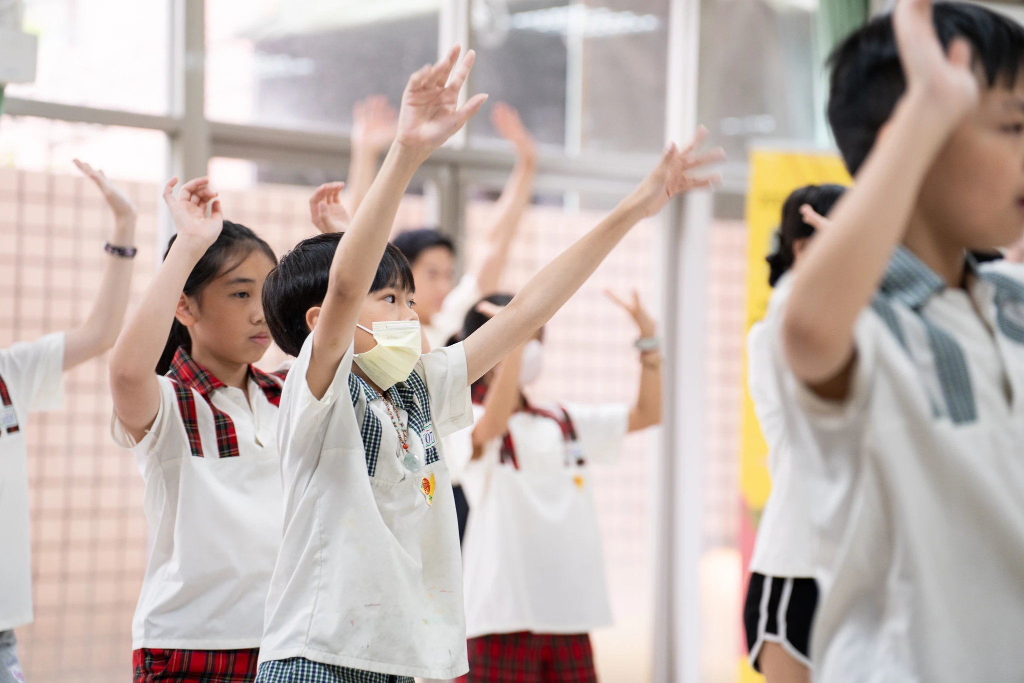 Young performers practising coordinated arm movements in a rehearsal room.