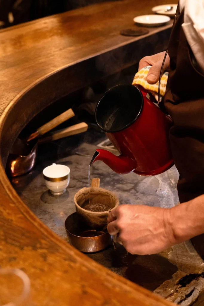 Barista pouring hot water through a cloth coffee filter behind a wooden counter.