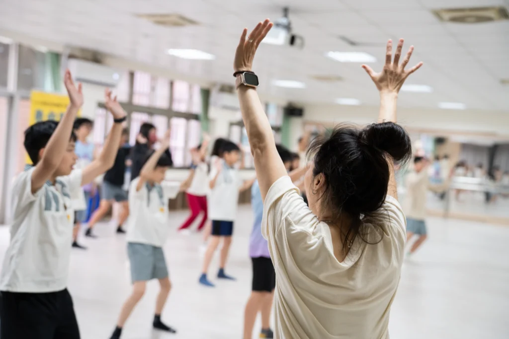 Children rehearsing with raised arms in a mirrored dance studio.
