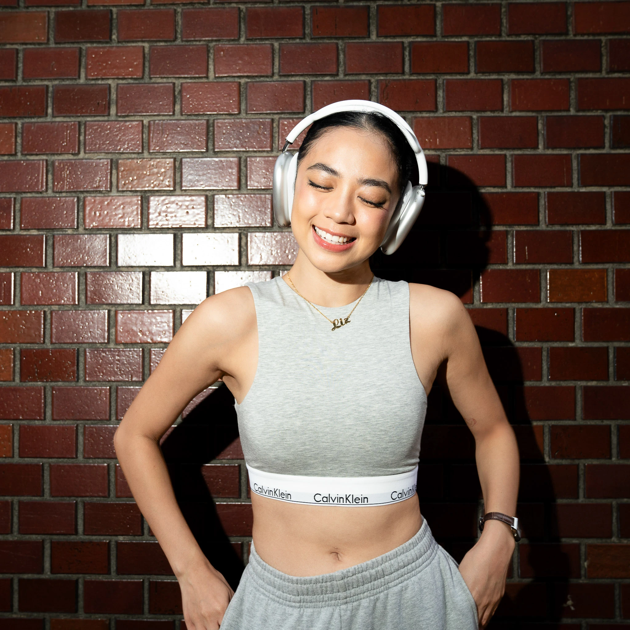 Smiling portrait in grey sportswear and headphones by a brick wall