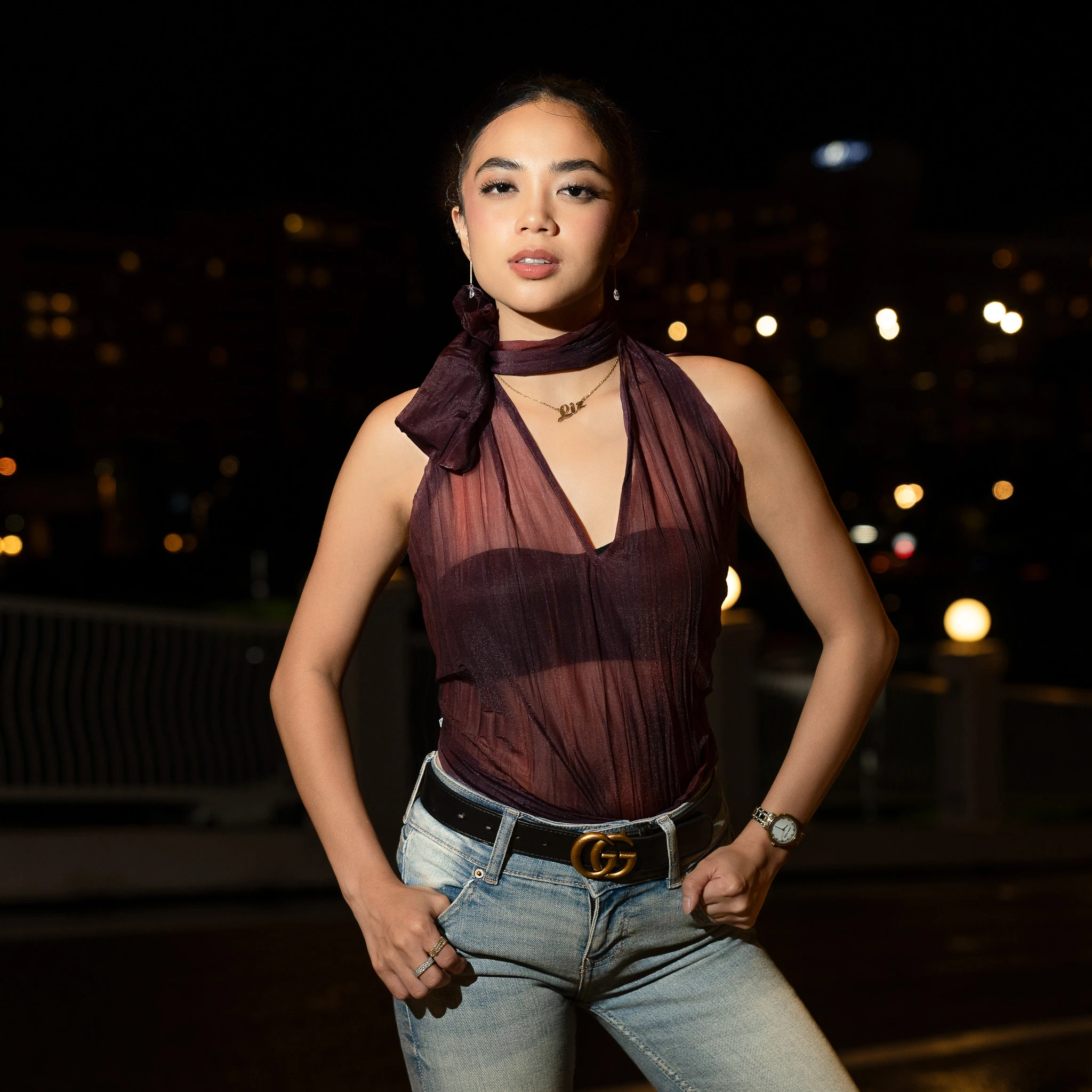 A front-facing night portrait showing earrings, a necklace and a tied burgundy top.