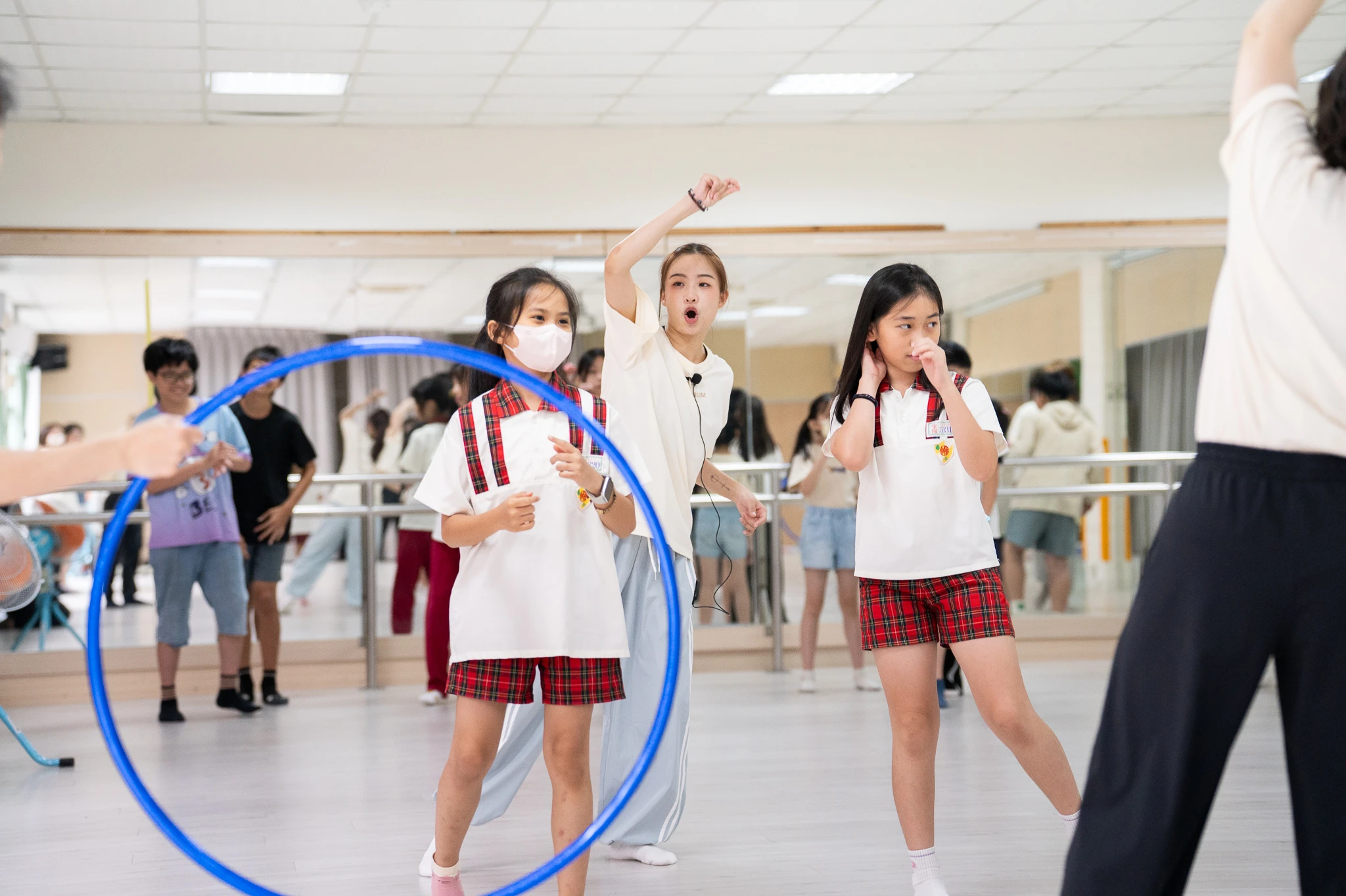 A facilitator demonstrates a movement with two students and a blue hoop in the foreground