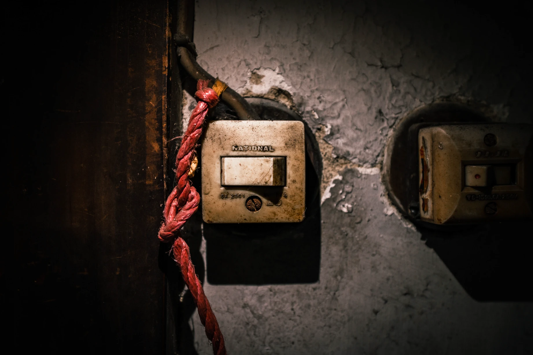 Two older switches and a red cord against a worn wall in the Kyoto machiya.