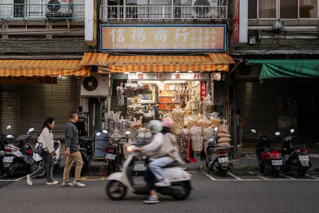 Scooter passing a traditional shopfront with a blue-and-gold sign.
