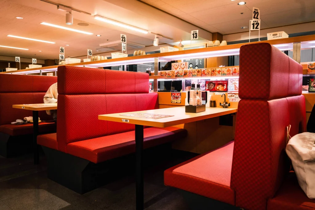 Empty red booth seats beside a restaurant's sushi conveyor.