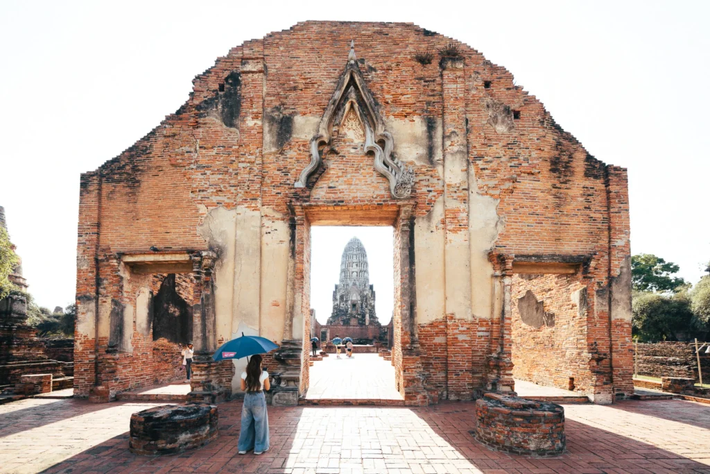 Brick temple gateway framing a distant tower, with visitors in the courtyard.