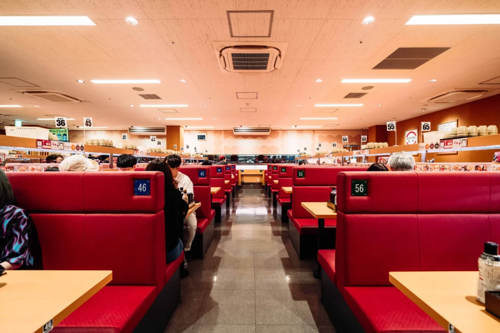 Rows of red booths inside a brightly lit sushi restaurant.