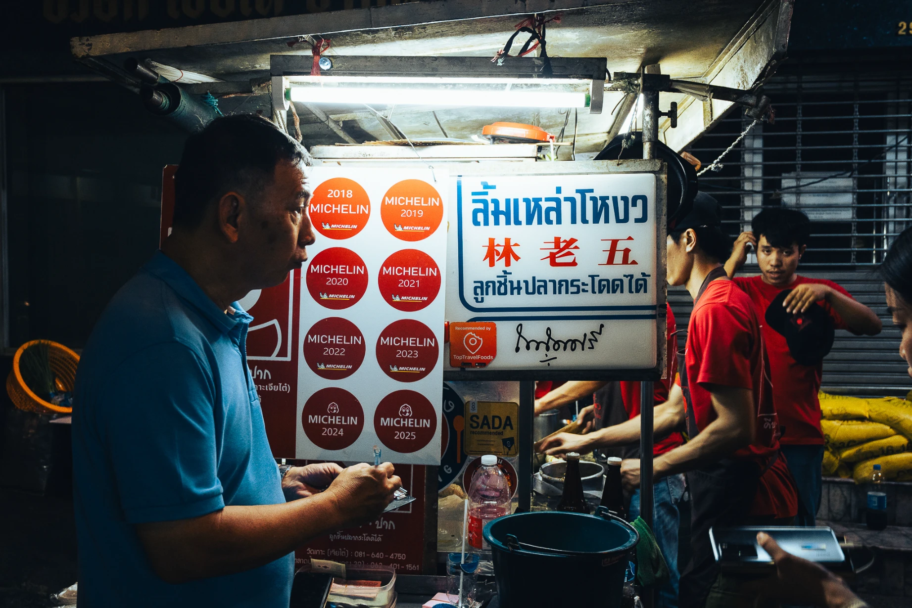 Street scene in Bangkok Chinatown with layered signs, traffic and pedestrians.