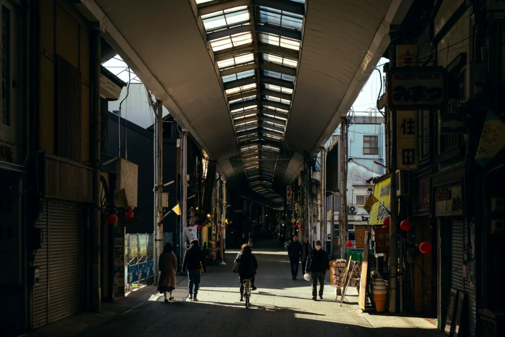 Pedestrians walking through a sunlit covered shopping arcade.