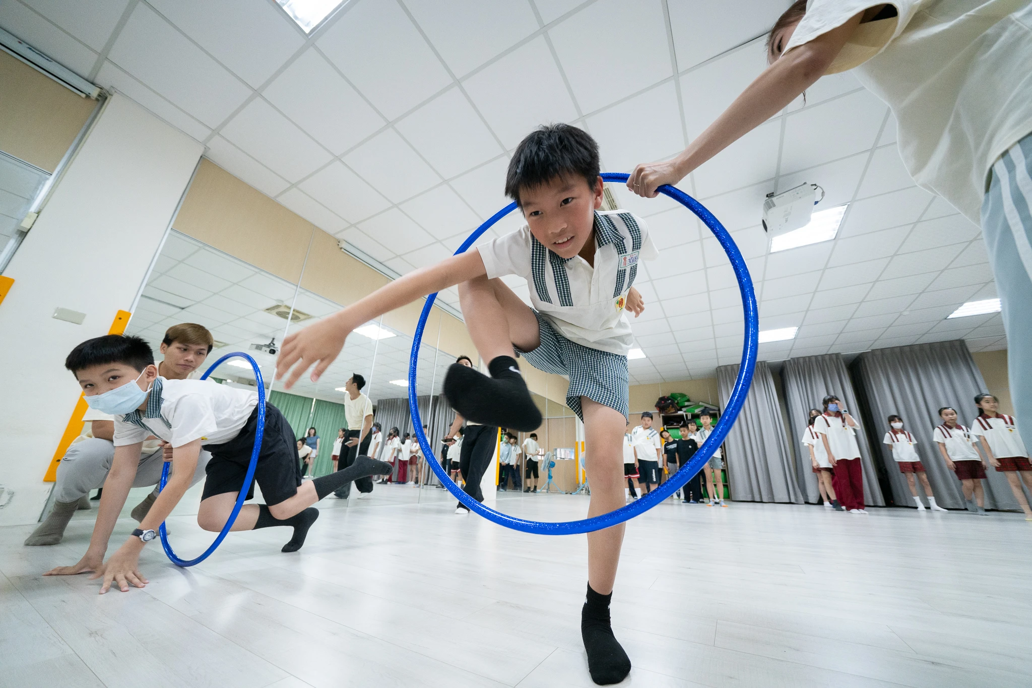 Students jumping through hoops in a bright rehearsal room.