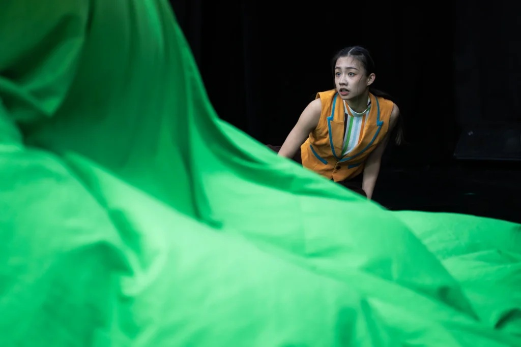 A performer drawing a large green cloth across a theatre floor.