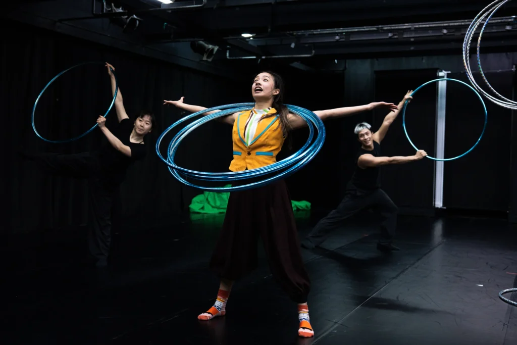 Hoop performers holding an ensemble pose in a dark rehearsal room.