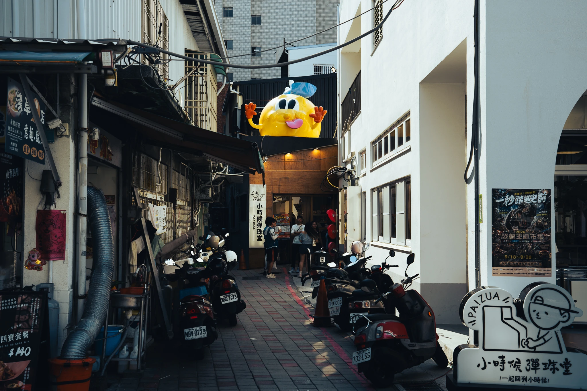 A narrow Tainan lane lined with shopfronts and parked scooters
