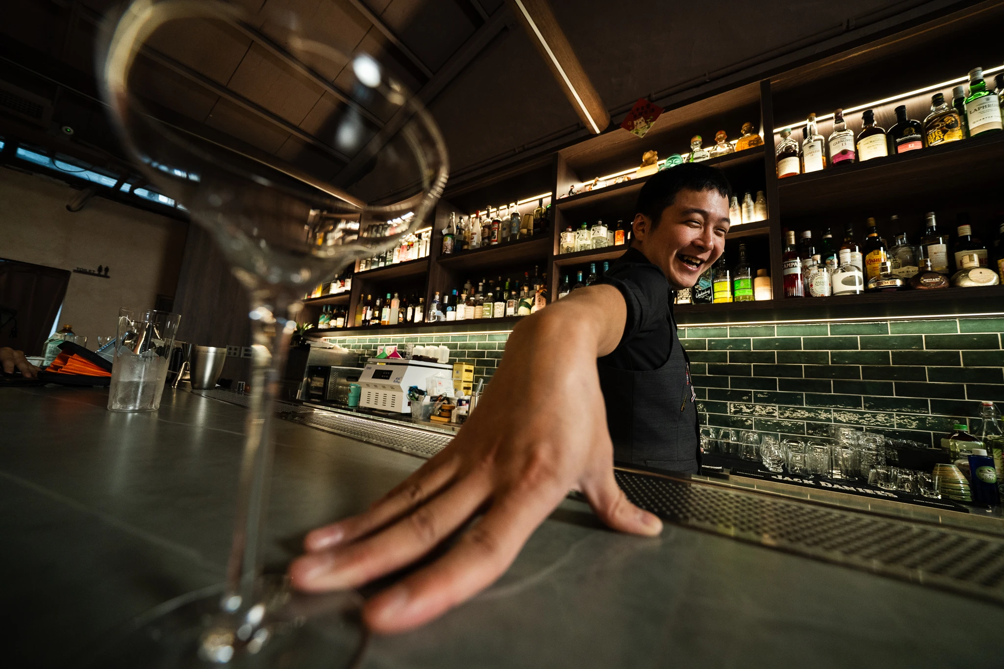 A smiling bartender reaching across the counter at Moonwell, with a glass in the foreground