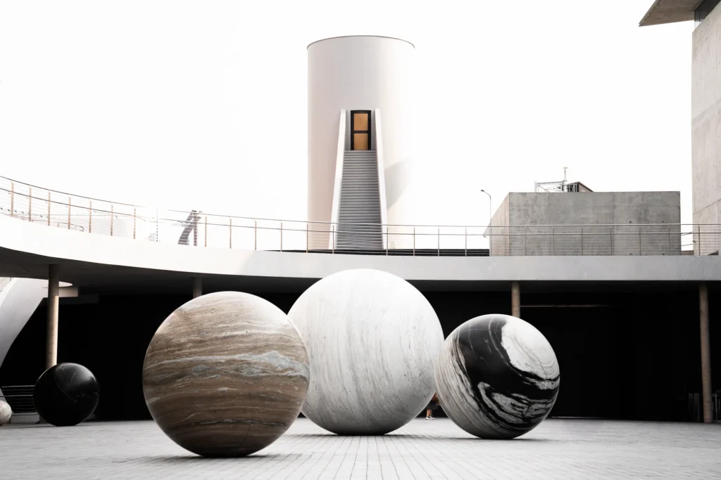 Large spherical sculptures arranged in a courtyard below a white tower.