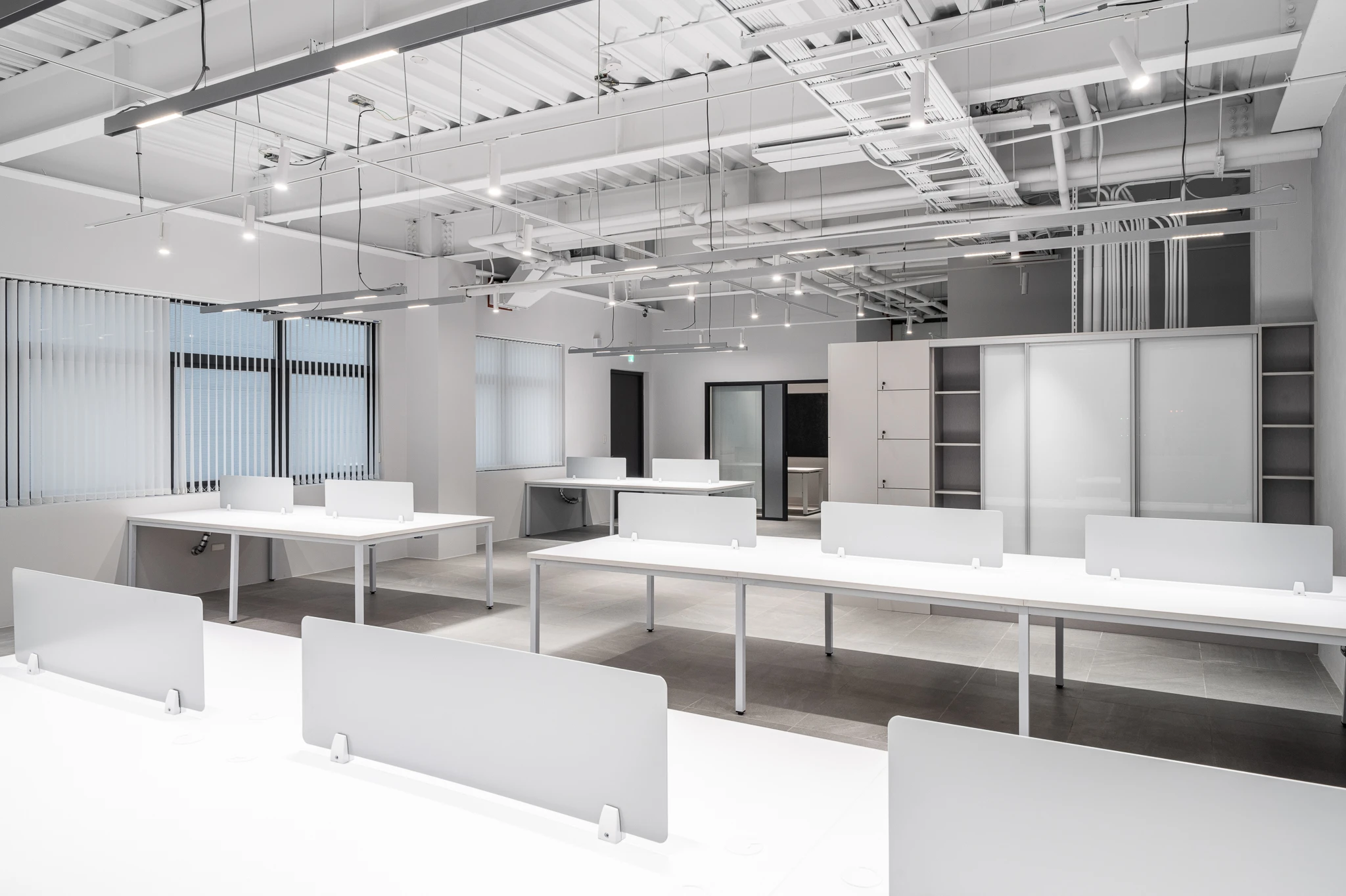 Open-plan office with pale desks and exposed ceiling services