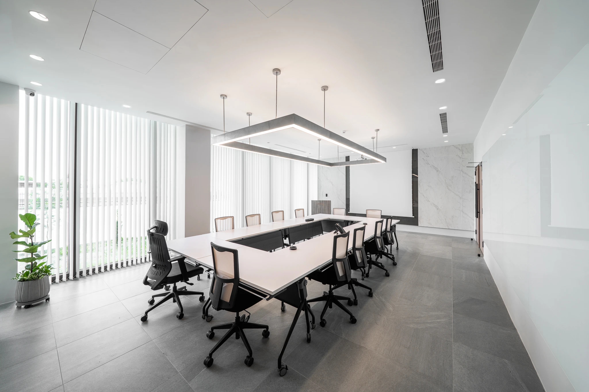 A meeting table and office chairs sit beside tall windows, with daylight falling across the table and floor.