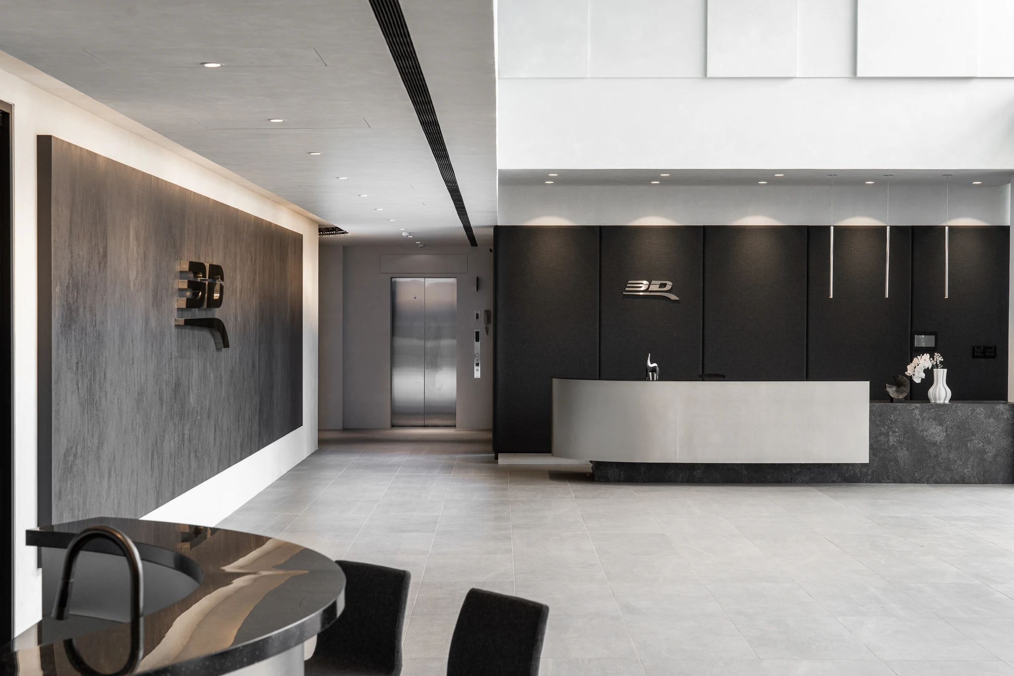 A reception counter beside a grey textured feature wall, with the edge of the workplace retained in the foreground.
