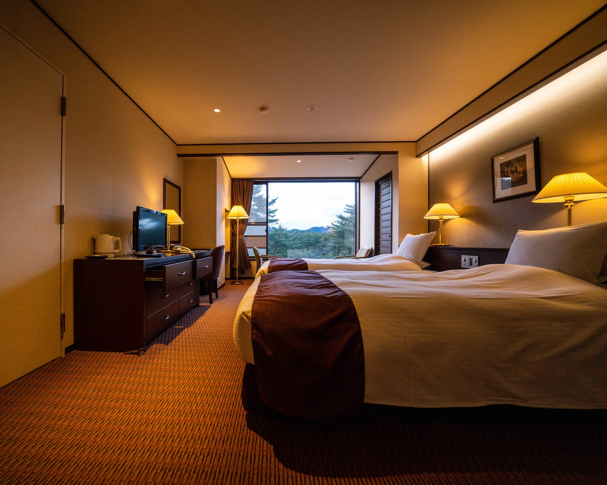 Twin guest room with warm lighting and a woodland view