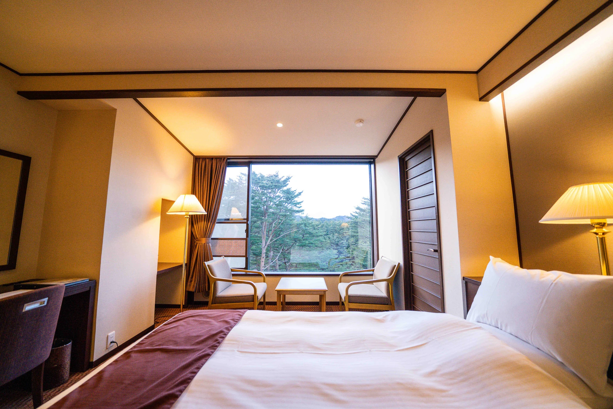 Guest bed beside a window framing pine trees