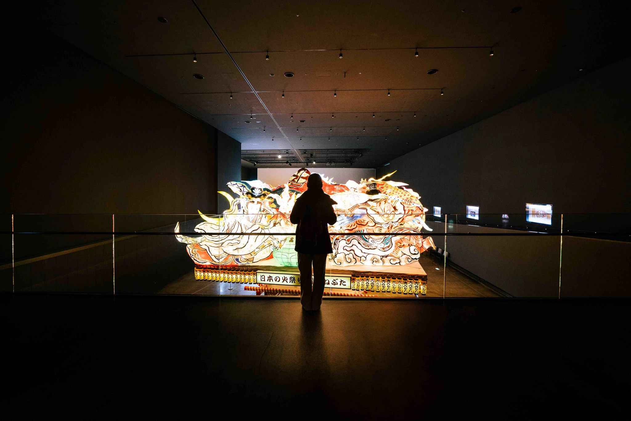 Visitor silhouetted before an illuminated Nebuta float