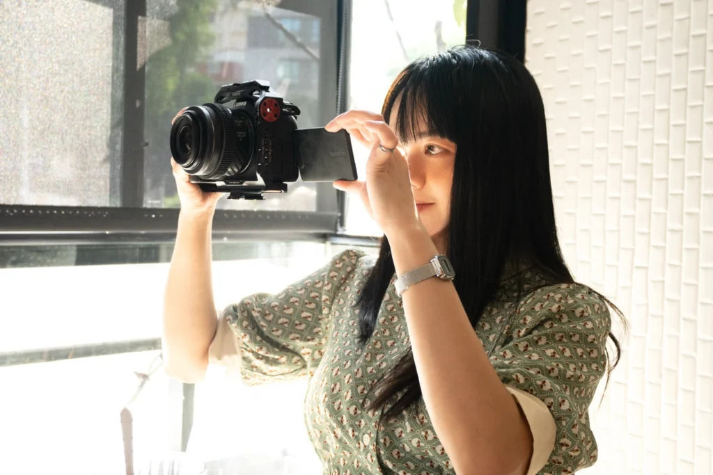 Person holding a camera beside a bright window.