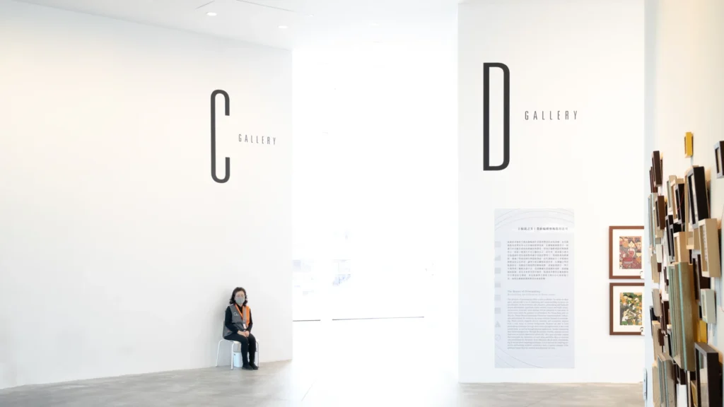 A visitor seated beside large lettered gallery entrances.