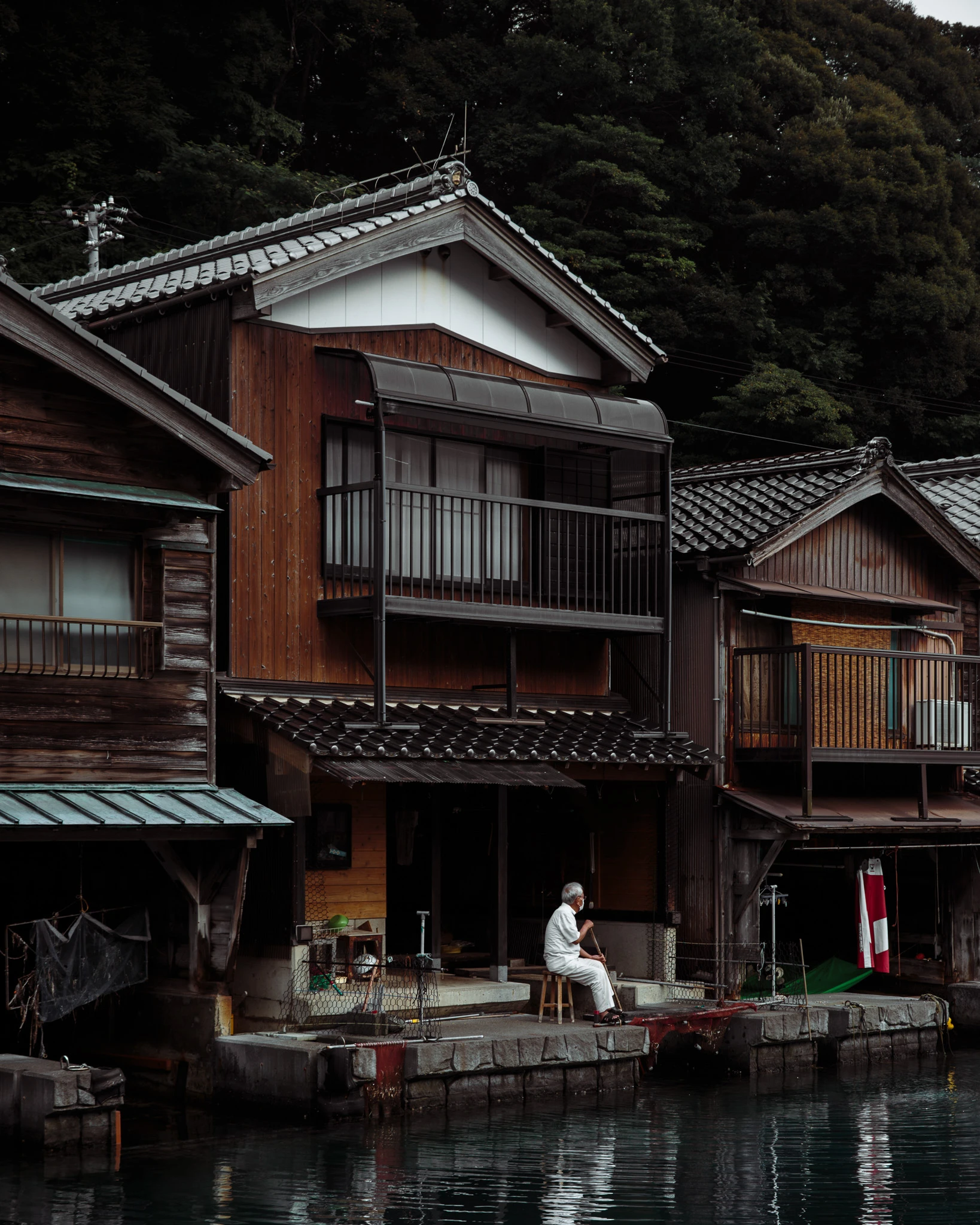 Person sitting beside a wooden boathouse facing the bay