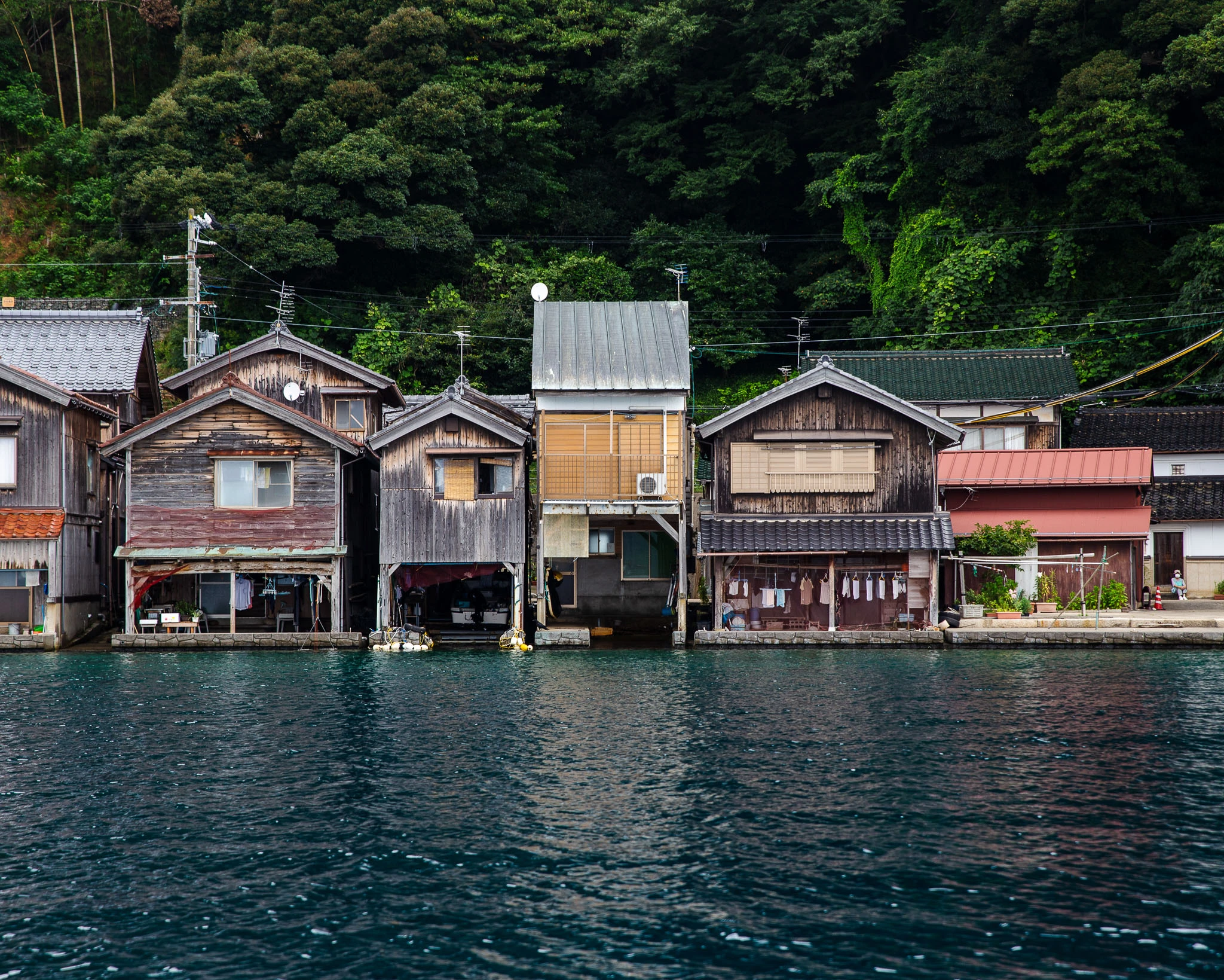 Row of boathouses below a wooded hillside