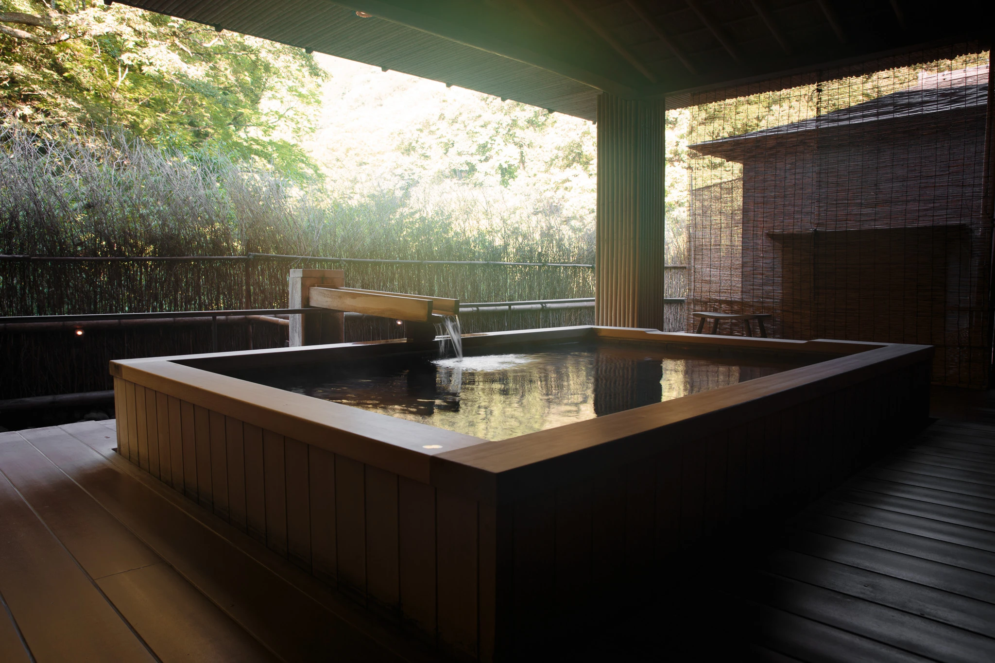 Timber bath beneath a roof with sunlight beyond