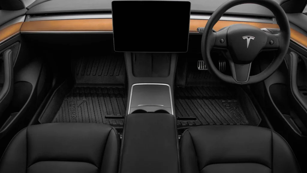 A Tesla cabin with fitted black floor mats and a central touchscreen.
